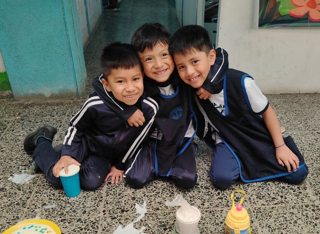 Three young boys in school uniform hug each other.
