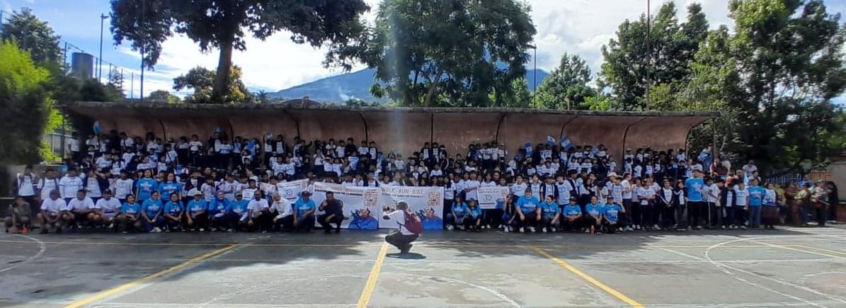 A large group picture of the Humanity First Masroor Ahmed School students and staff outside on a blacktop basketball court.
